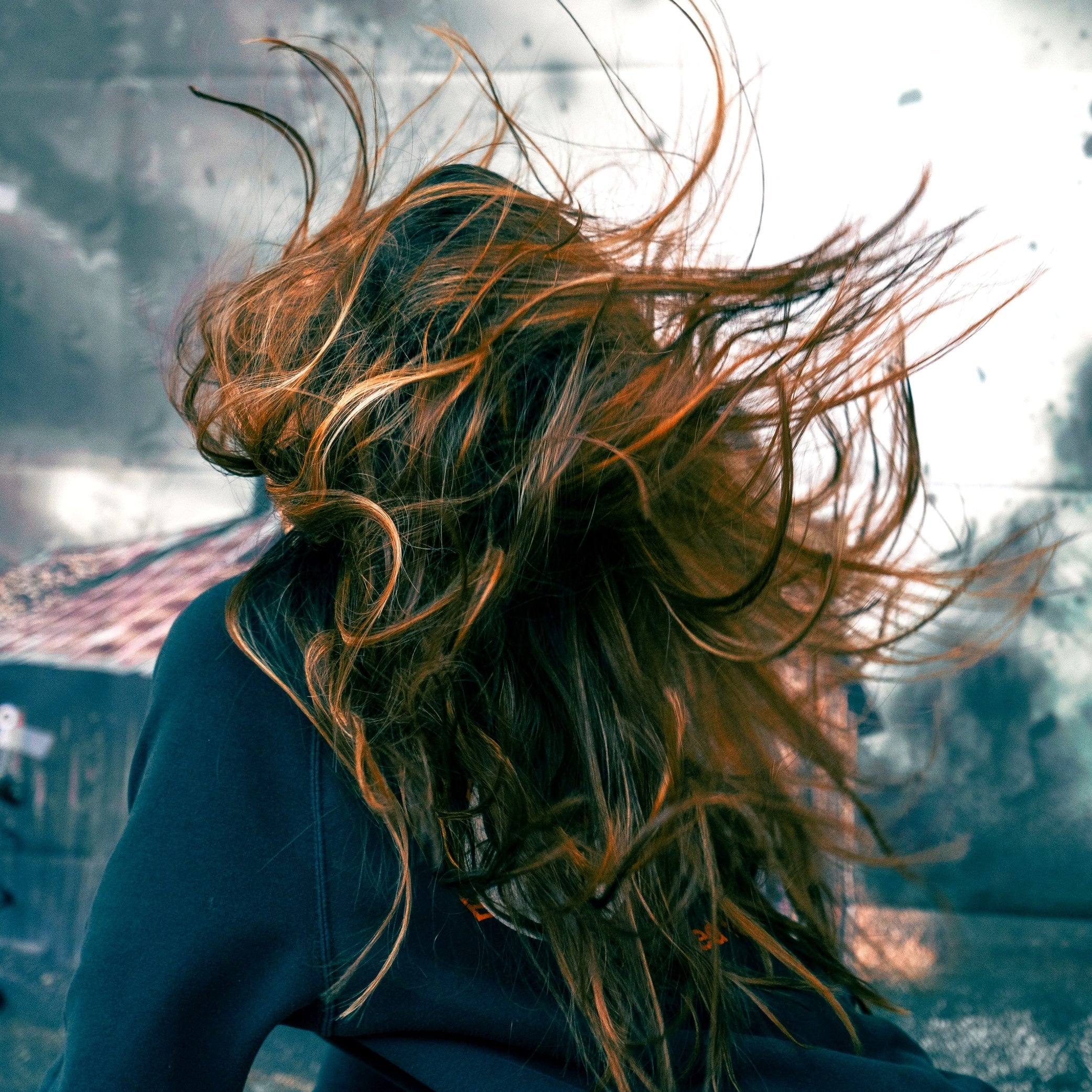 Women with long brown and red hair walking into a storm